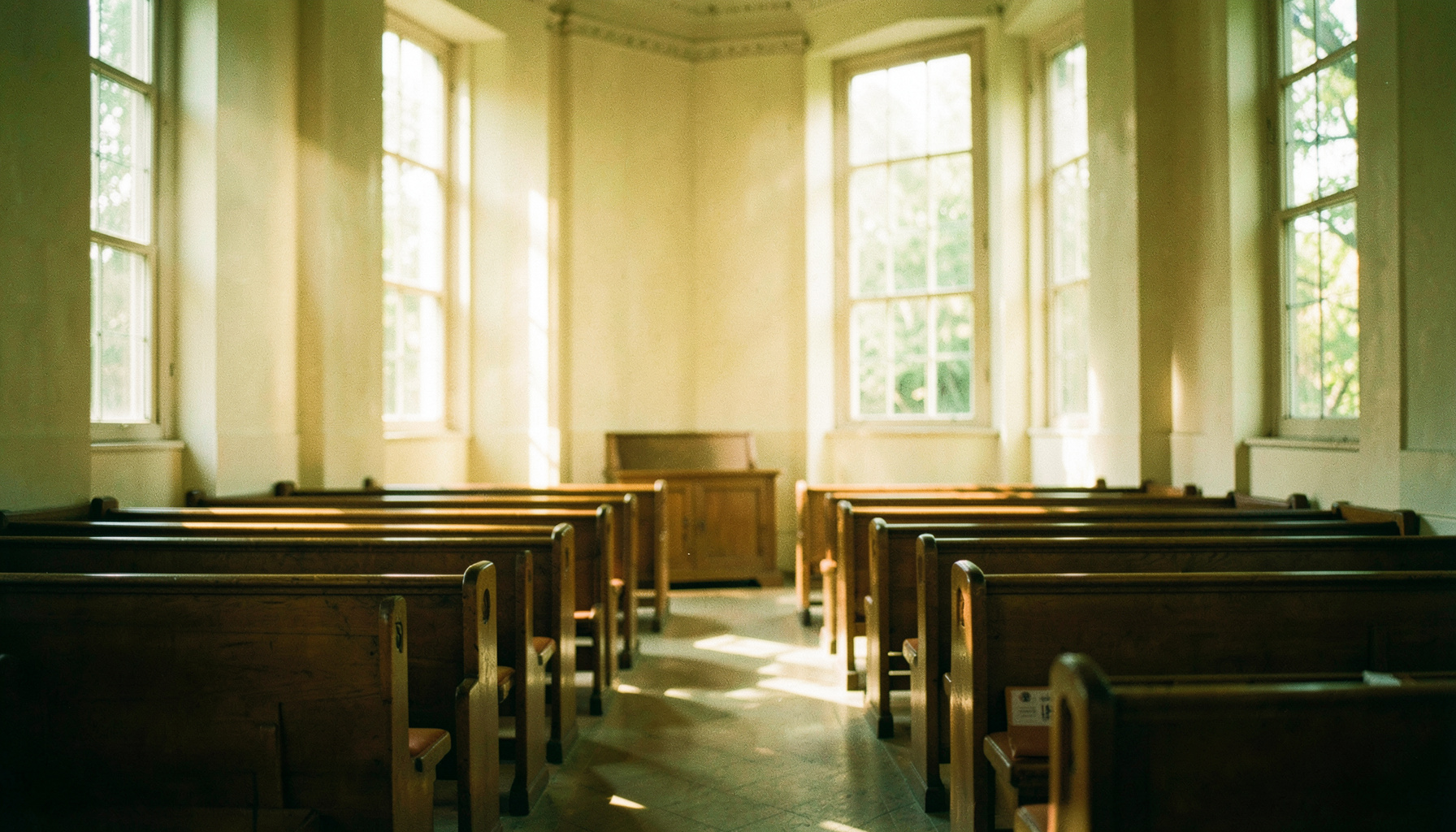 Warm morning light streaming through tall windows into a quiet sanctuary with wooden pews, soft amber and cream tones, peaceful and welcoming atmosphere